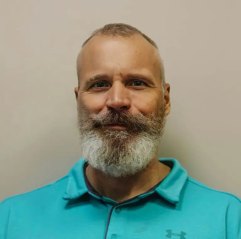 Dr. Tom Jensen smiling, with a full grey beard and a teal polo shirt