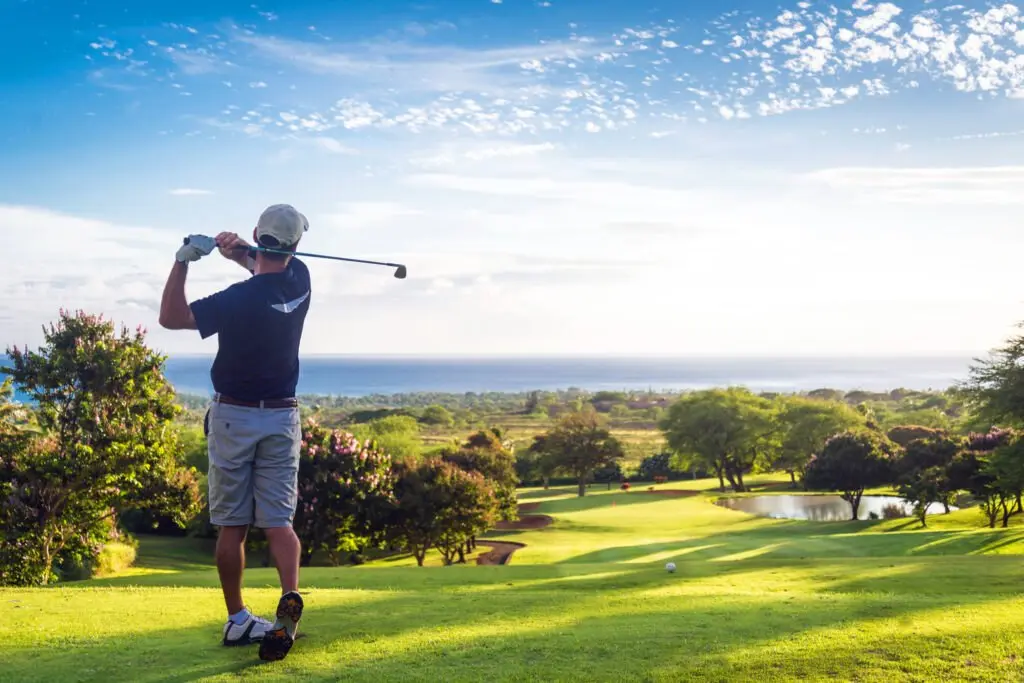A golfer finishing a swing on a green course under a blue sky